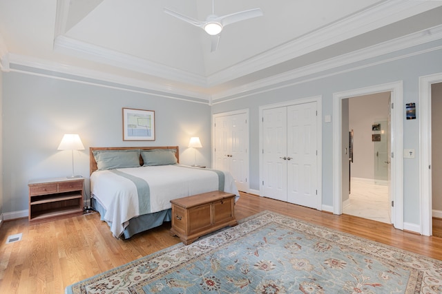 bedroom with ornamental molding, light wood-type flooring, multiple closets, and ceiling fan