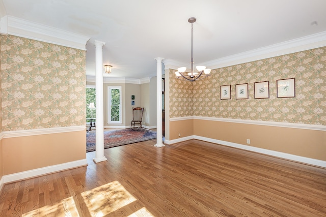 empty room with ornate columns, a notable chandelier, crown molding, and hardwood / wood-style floors