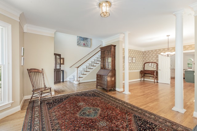 living area featuring ornamental molding, light wood-type flooring, decorative columns, and a notable chandelier