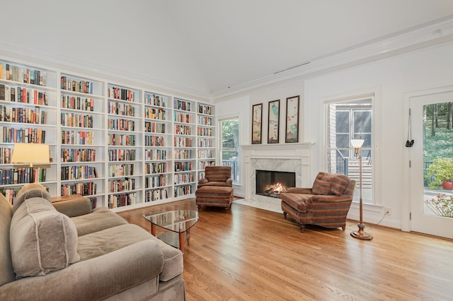 living area with ornamental molding, light wood-type flooring, vaulted ceiling, and a high end fireplace