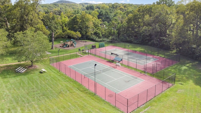 view of tennis court with a playground and a lawn