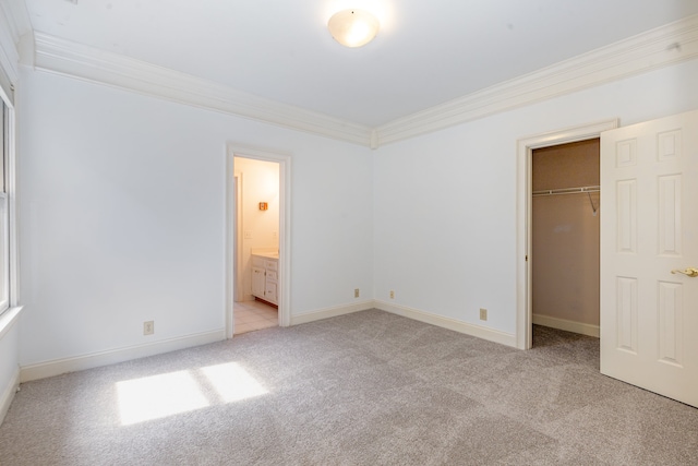 unfurnished bedroom featuring ornamental molding, ensuite bath, light carpet, and a walk in closet