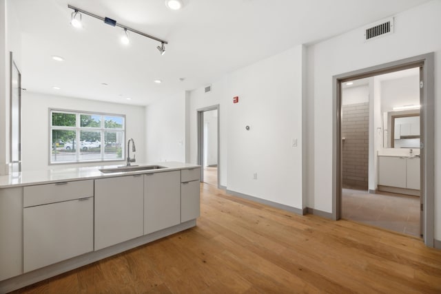 kitchen featuring rail lighting, white cabinetry, light hardwood / wood-style floors, and sink