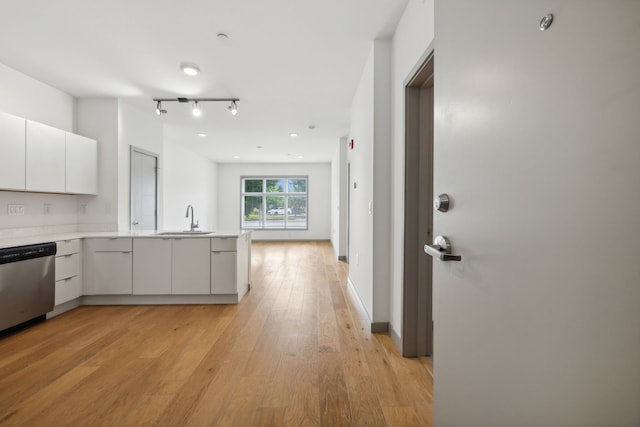 kitchen featuring white cabinets, sink, kitchen peninsula, stainless steel dishwasher, and light wood-type flooring