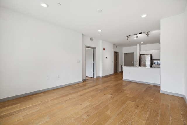 unfurnished living room with light wood-type flooring, sink, and track lighting