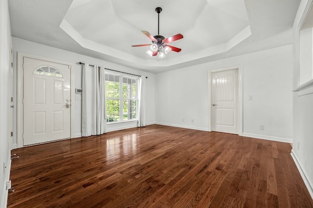 unfurnished living room featuring dark wood-type flooring, ceiling fan, and a raised ceiling