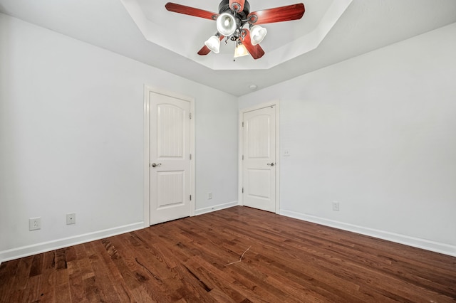 empty room featuring ceiling fan, a raised ceiling, and wood-type flooring