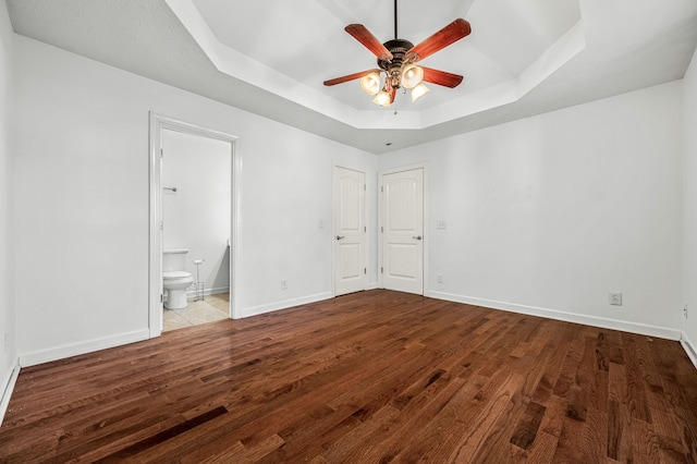 unfurnished bedroom with connected bathroom, ceiling fan, a tray ceiling, and light hardwood / wood-style flooring