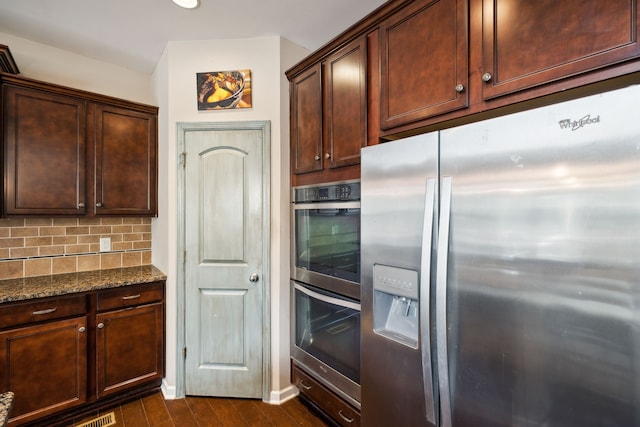 kitchen featuring dark wood-type flooring, tasteful backsplash, stainless steel appliances, dark brown cabinetry, and dark stone counters