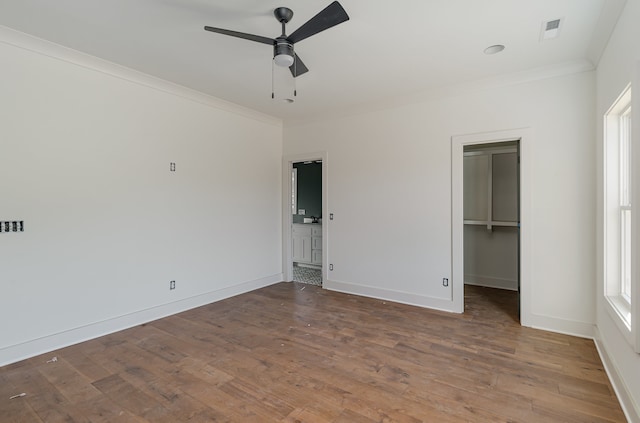 unfurnished bedroom featuring hardwood / wood-style floors, ceiling fan, a spacious closet, ornamental molding, and a closet