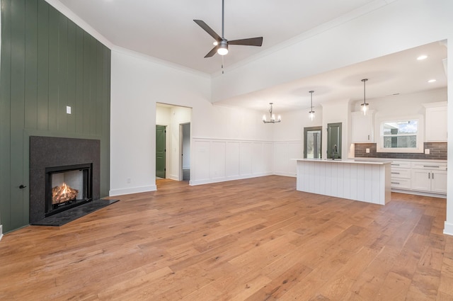 unfurnished living room with crown molding, a large fireplace, ceiling fan with notable chandelier, and light wood-type flooring