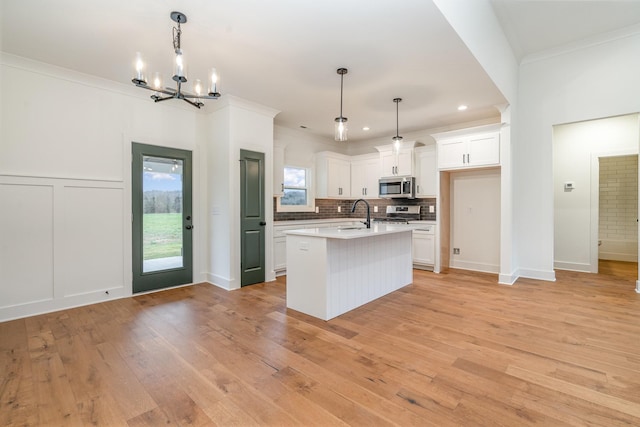 kitchen with appliances with stainless steel finishes, ornamental molding, a kitchen island with sink, decorative light fixtures, and white cabinetry