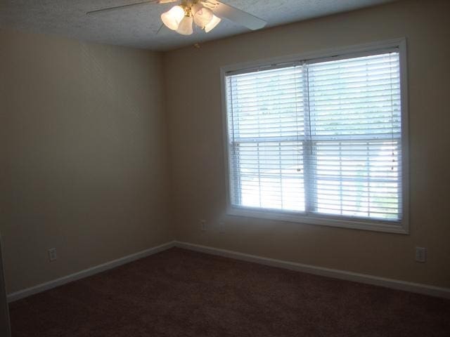 spare room with dark colored carpet, ceiling fan, and a textured ceiling