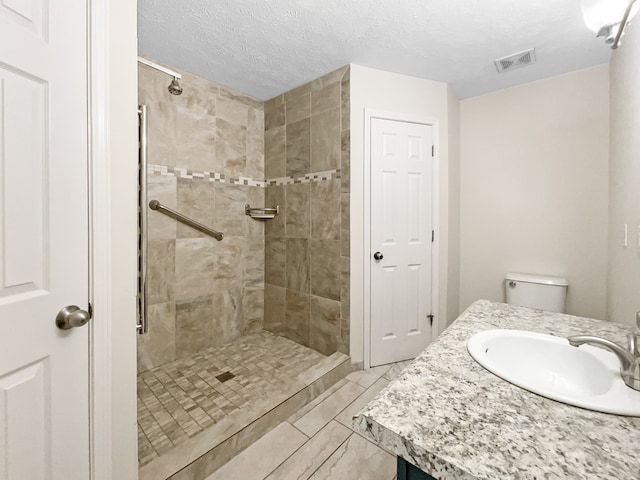 bathroom with a tile shower, a textured ceiling, vanity, and toilet