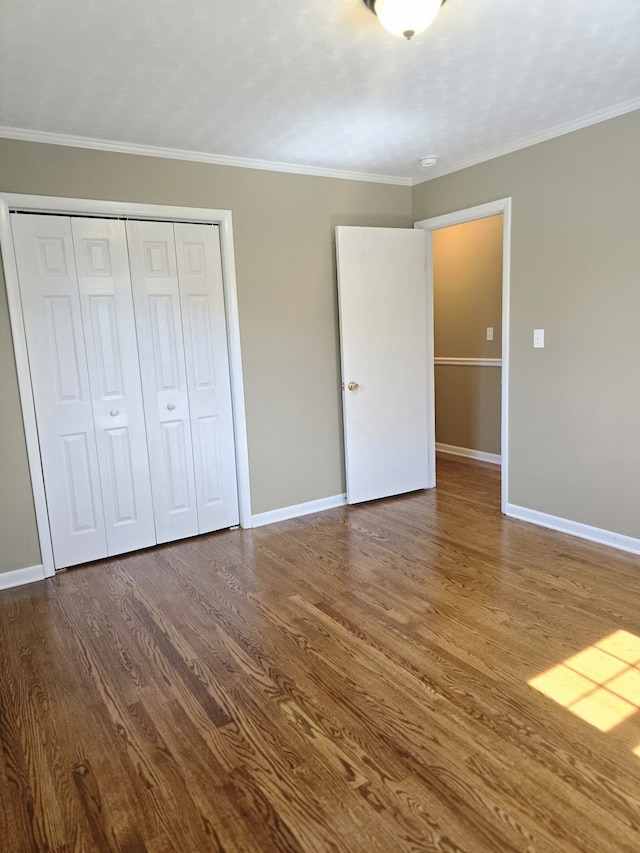 unfurnished bedroom with a closet, crown molding, and hardwood / wood-style floors