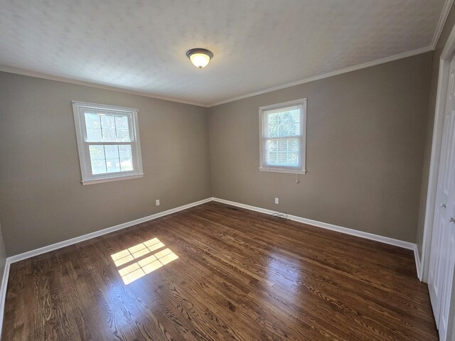 empty room featuring crown molding, dark wood-type flooring, and plenty of natural light