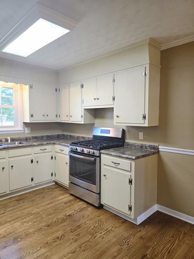 kitchen featuring light wood-type flooring, crown molding, white cabinetry, and stainless steel gas range