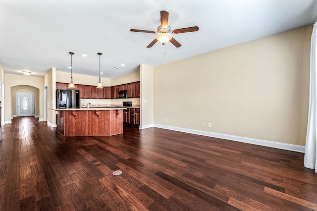 kitchen with a center island with sink, decorative light fixtures, dark wood-type flooring, black appliances, and a breakfast bar