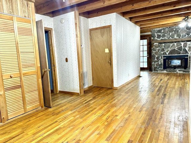 unfurnished living room with wallpapered walls, a stone fireplace, visible vents, wood-type flooring, and beam ceiling