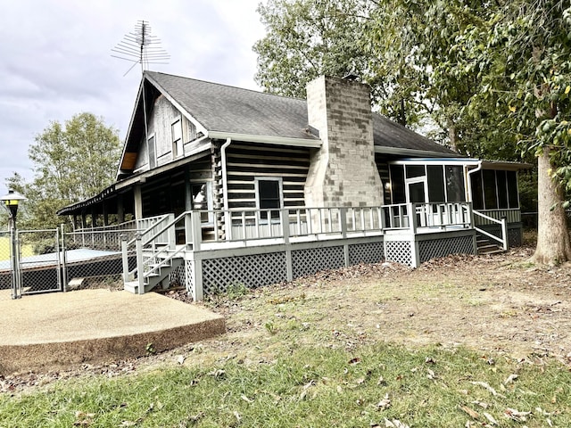 rear view of property featuring a chimney, a gate, roof with shingles, a wooden deck, and a sunroom