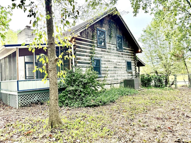 view of property exterior with central air condition unit, a sunroom, and fence
