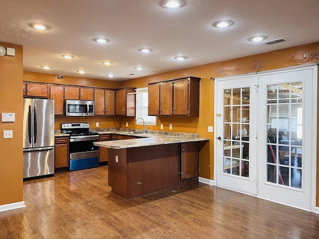 kitchen with stainless steel appliances, kitchen peninsula, hardwood / wood-style flooring, and a textured ceiling