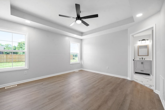 unfurnished bedroom featuring connected bathroom, wood-type flooring, a tray ceiling, ceiling fan, and sink