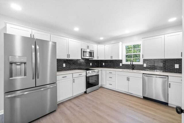 kitchen with appliances with stainless steel finishes, white cabinets, backsplash, light hardwood / wood-style flooring, and sink