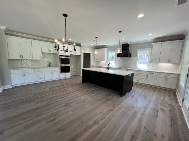 kitchen featuring pendant lighting, white cabinetry, custom range hood, a center island with sink, and hardwood / wood-style floors