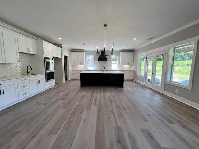 kitchen featuring white cabinets, backsplash, stainless steel double oven, decorative light fixtures, and hardwood / wood-style floors