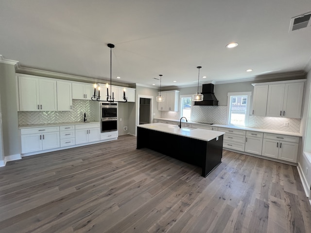 kitchen with hardwood / wood-style floors, hanging light fixtures, custom range hood, and white cabinetry