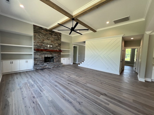 unfurnished living room featuring ceiling fan, built in features, beam ceiling, a stone fireplace, and hardwood / wood-style floors