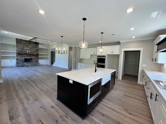 kitchen featuring a stone fireplace, a center island with sink, decorative light fixtures, white cabinetry, and light hardwood / wood-style floors