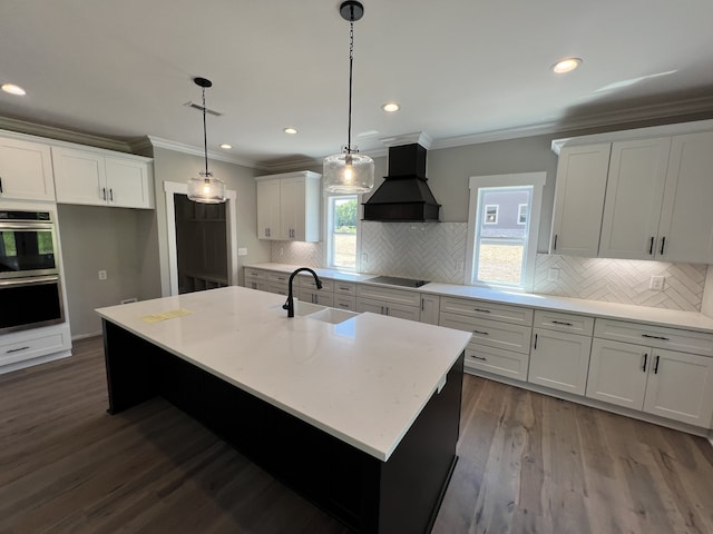 kitchen featuring sink, an island with sink, custom range hood, decorative light fixtures, and dark hardwood / wood-style flooring