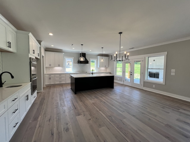 kitchen with custom exhaust hood, hanging light fixtures, sink, white cabinetry, and hardwood / wood-style flooring