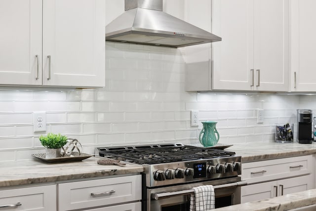 kitchen with high end stainless steel range, light stone countertops, wall chimney exhaust hood, and white cabinets