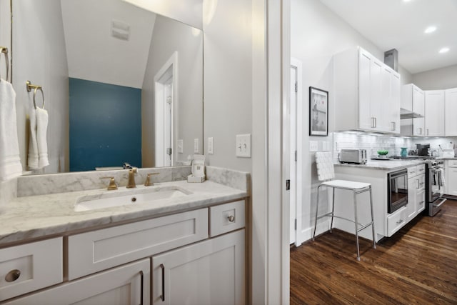 bathroom with wood-type flooring, backsplash, sink, and vaulted ceiling