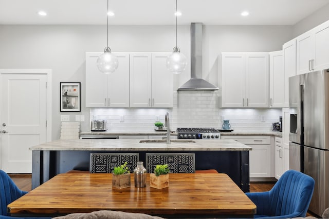 kitchen featuring white cabinets, hanging light fixtures, sink, wall chimney range hood, and stainless steel appliances