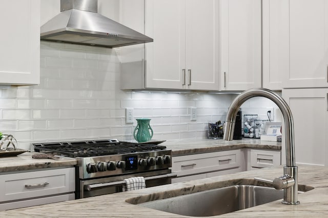 kitchen with light stone counters, white cabinets, wall chimney range hood, decorative backsplash, and stainless steel range