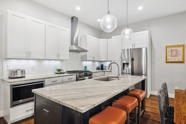 kitchen featuring white cabinets, a center island with sink, wall chimney exhaust hood, appliances with stainless steel finishes, and dark hardwood / wood-style floors