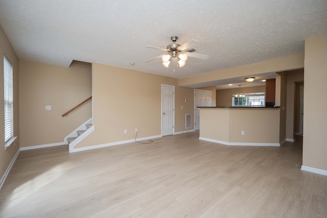 unfurnished living room with ceiling fan with notable chandelier, a textured ceiling, and light hardwood / wood-style flooring