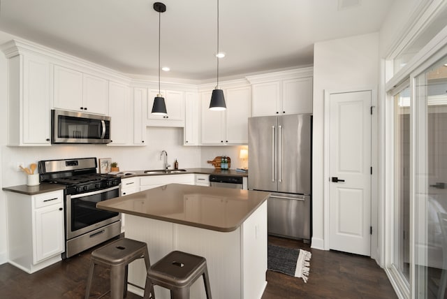 kitchen with hanging light fixtures, a kitchen island, white cabinetry, appliances with stainless steel finishes, and dark hardwood / wood-style floors