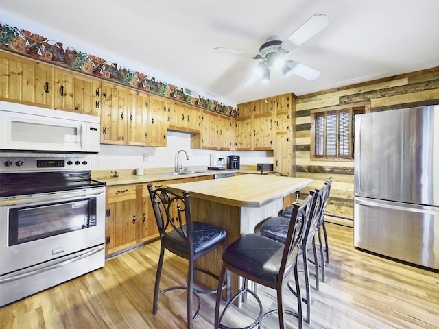 kitchen featuring light hardwood / wood-style flooring, wooden walls, a baseboard radiator, appliances with stainless steel finishes, and ceiling fan