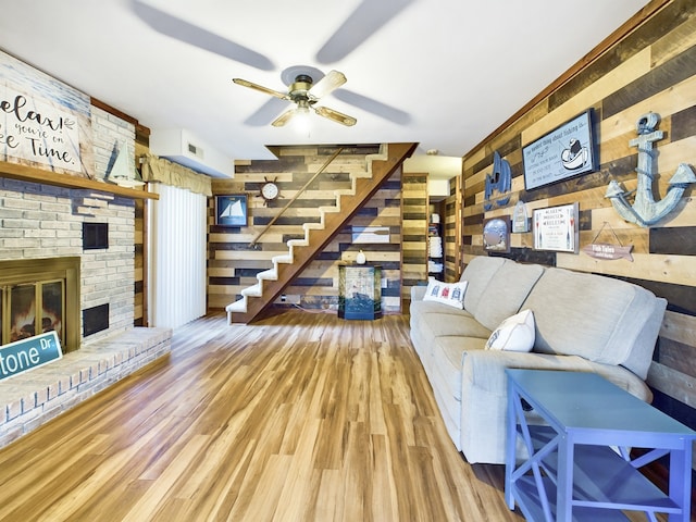 living room featuring light hardwood / wood-style flooring, a brick fireplace, wood walls, and ceiling fan