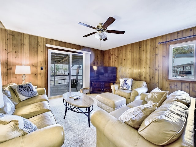 living room featuring carpet, wood walls, ceiling fan, and a healthy amount of sunlight