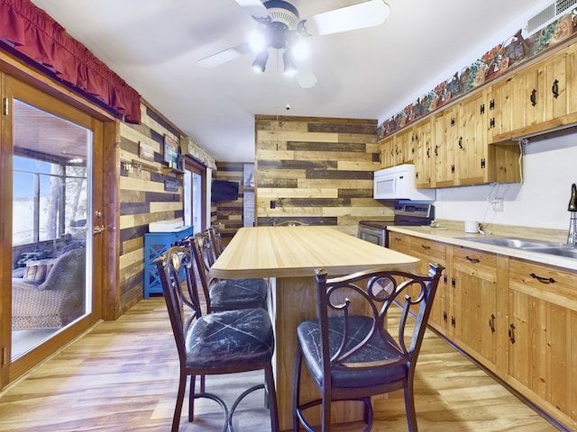 kitchen featuring light hardwood / wood-style flooring, wood walls, ceiling fan, and stainless steel electric range