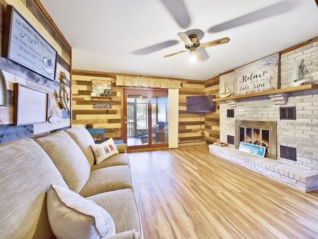 living room featuring ceiling fan, wooden walls, a fireplace, and wood-type flooring