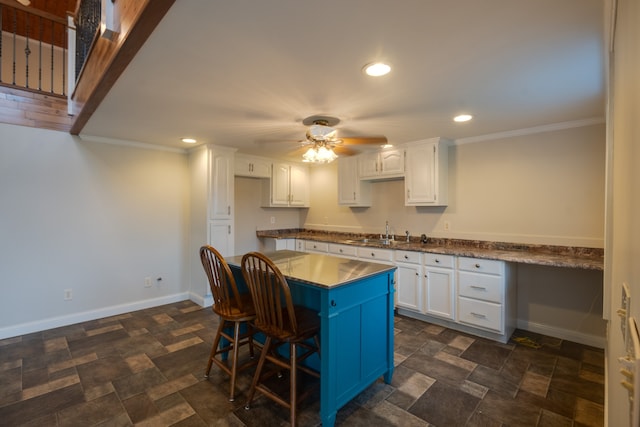 kitchen with ceiling fan, ornamental molding, sink, white cabinetry, and a kitchen breakfast bar