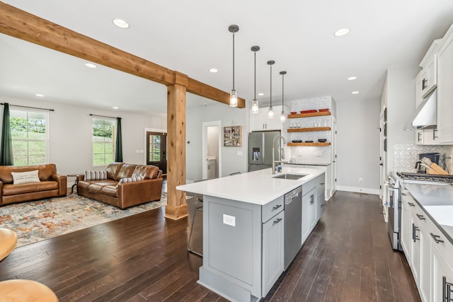 kitchen with white cabinets, an island with sink, pendant lighting, dark wood-type flooring, and stainless steel appliances