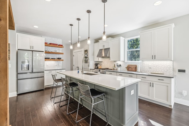 kitchen with dark hardwood / wood-style floors, an island with sink, white cabinets, stainless steel appliances, and decorative light fixtures